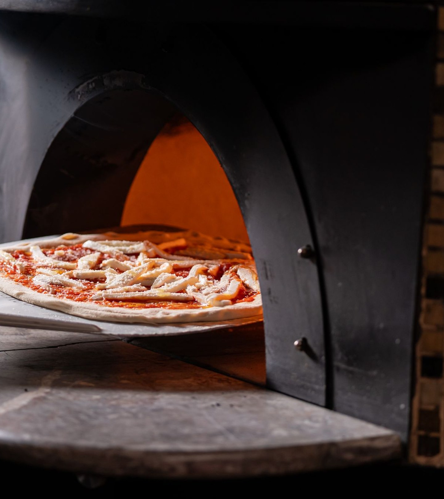 Una pizza artigianale viene infornata nel forno a legna
