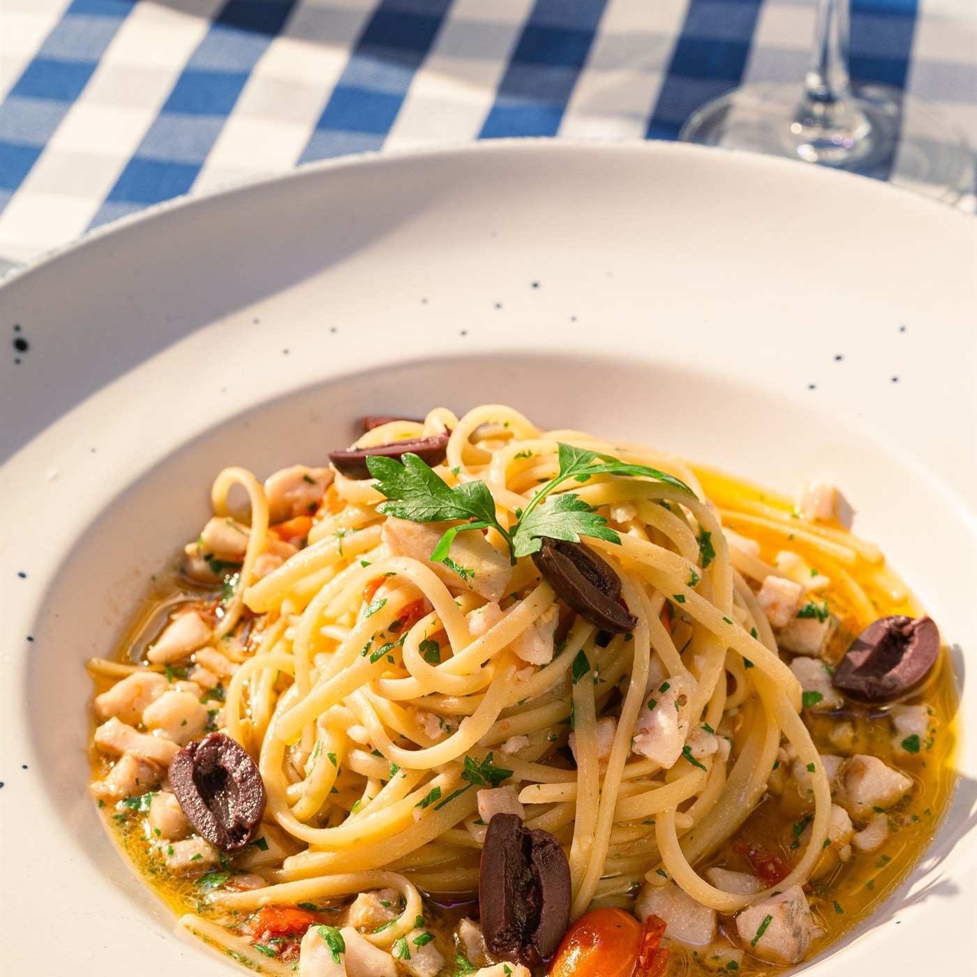 Piatto di pasta ai frutti di mare con olive e calice di vino